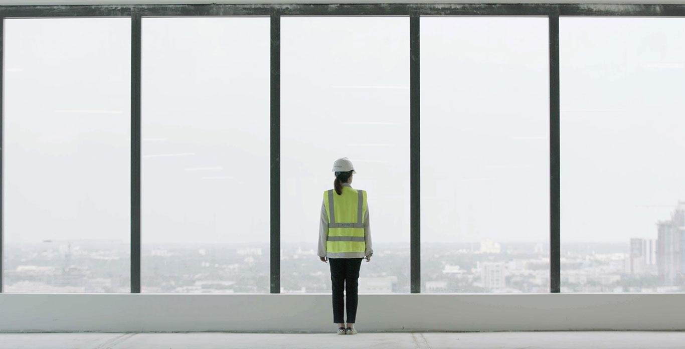 Adriana Cisneros wearing a high visibility jacket looking out of a high rise building window 